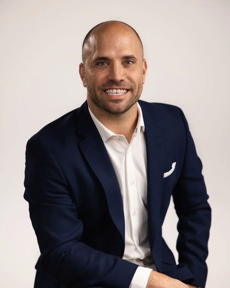 Adam Kayce, Home Shows host, in a navy blazer and white shirt against a light gray background