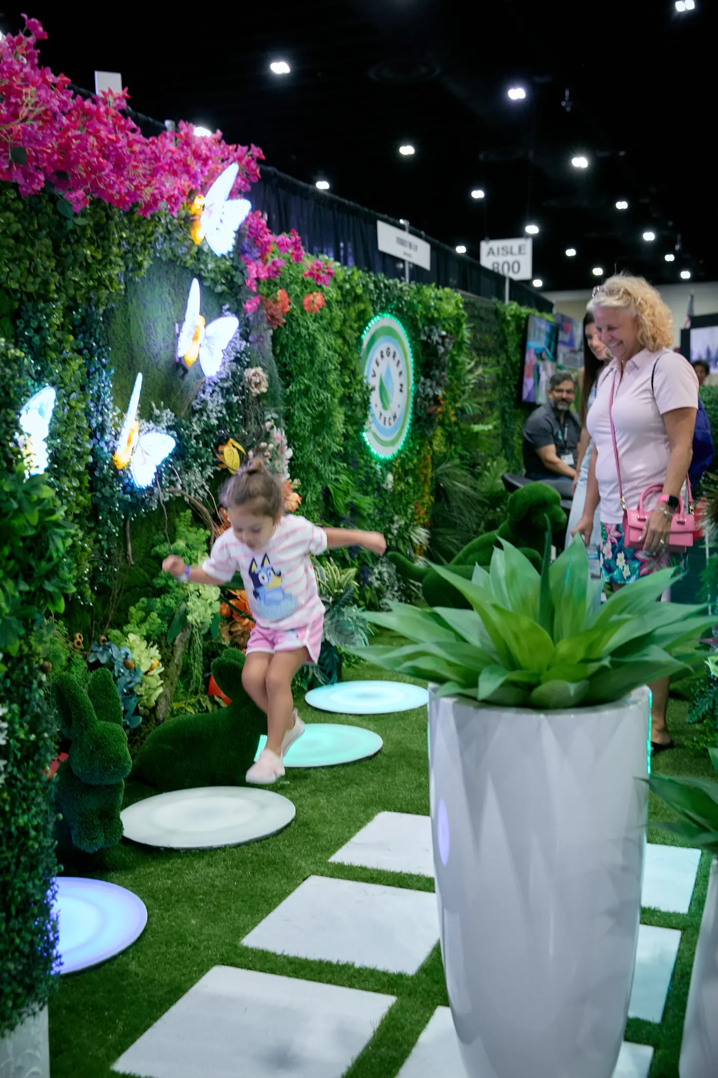 Child hopping across glowing stepping-stones through a lush indoor garden booth