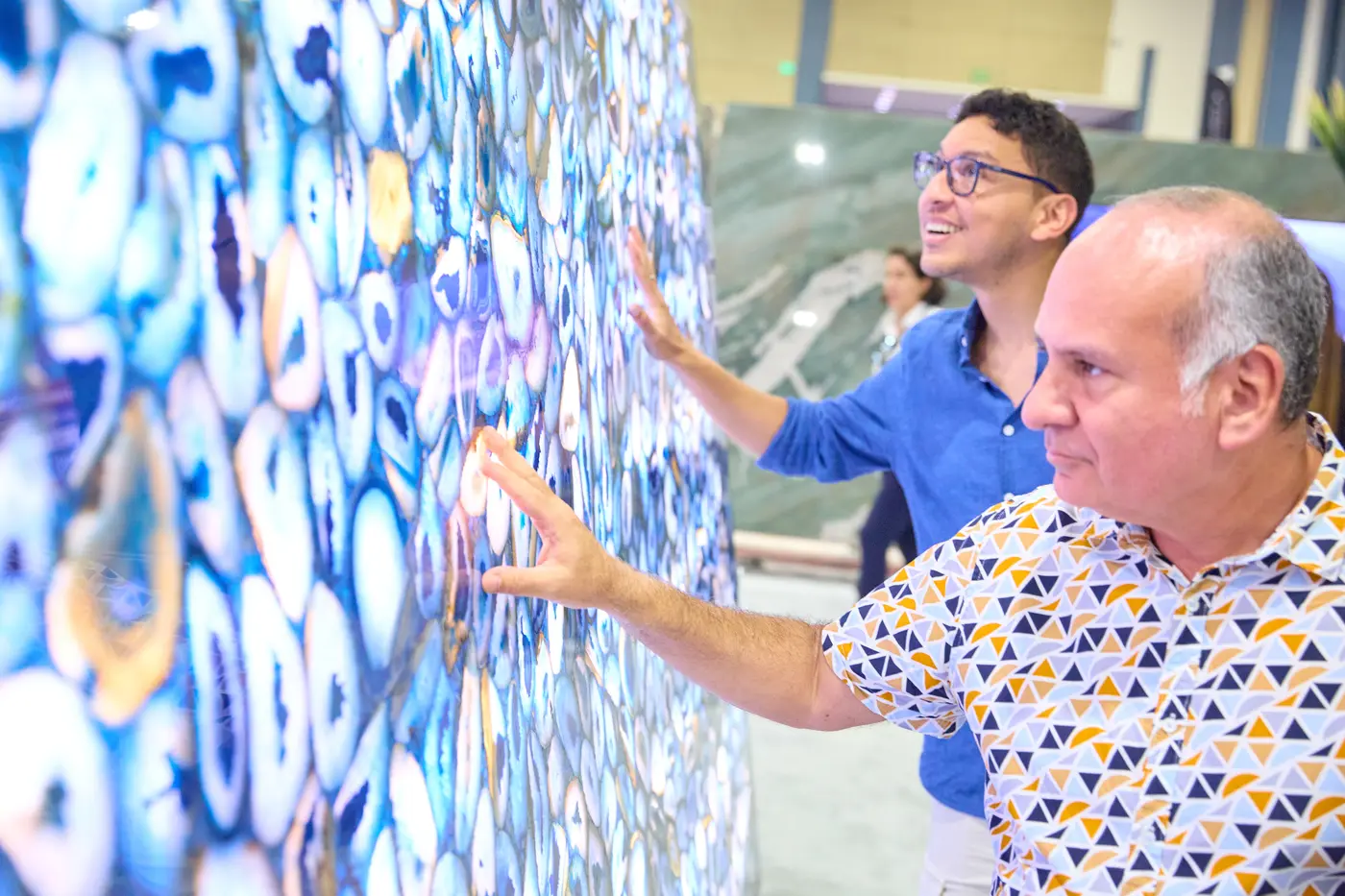 Two men examining a backlit blue agate stone slab wall