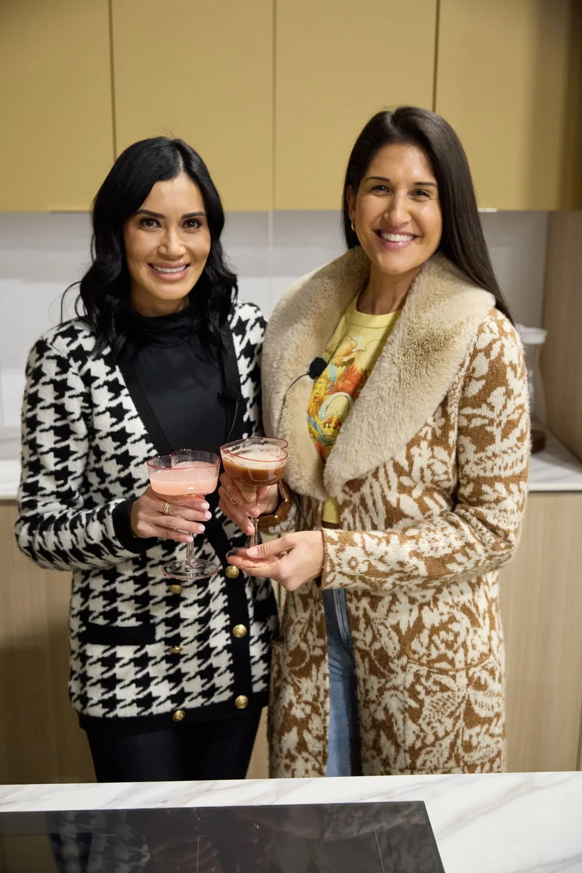 Two women toasting with pink cocktails in a kitchen display booth at a home show