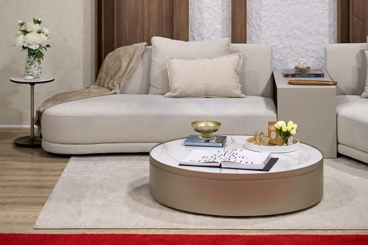 Neutral-toned living room vignette with curved sofa, round marble coffee table, and floral accent
