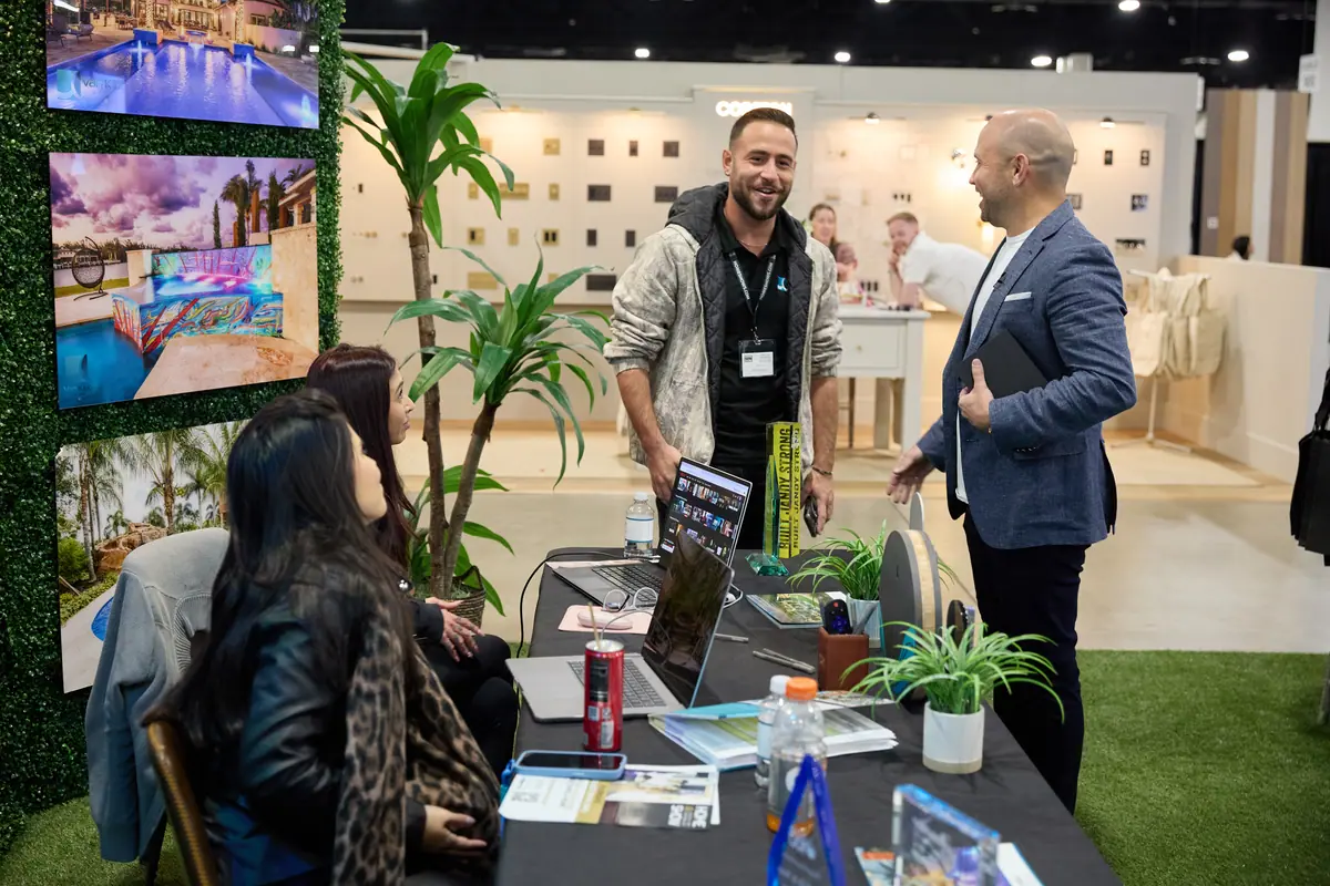 Pool company booth staff chatting with a show host, pool imagery on TV screens behind them