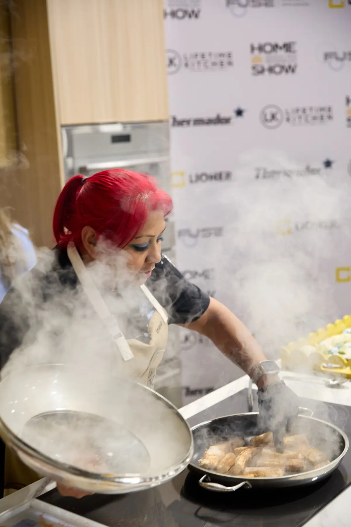 Chef with red hair cooking over a steaming skillet at a Home Design Show culinary stage