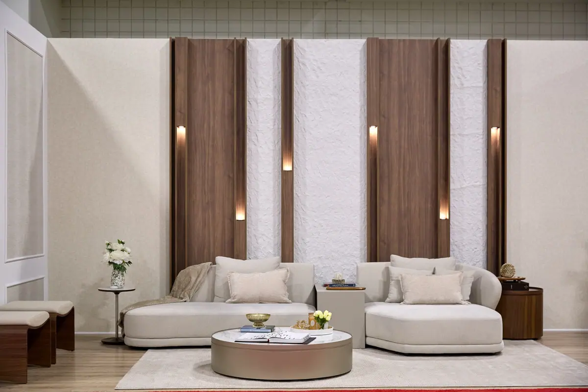 Luxury living room vignette with curved cream sofas, walnut wood panels, and backlit sconces at a design exhibit