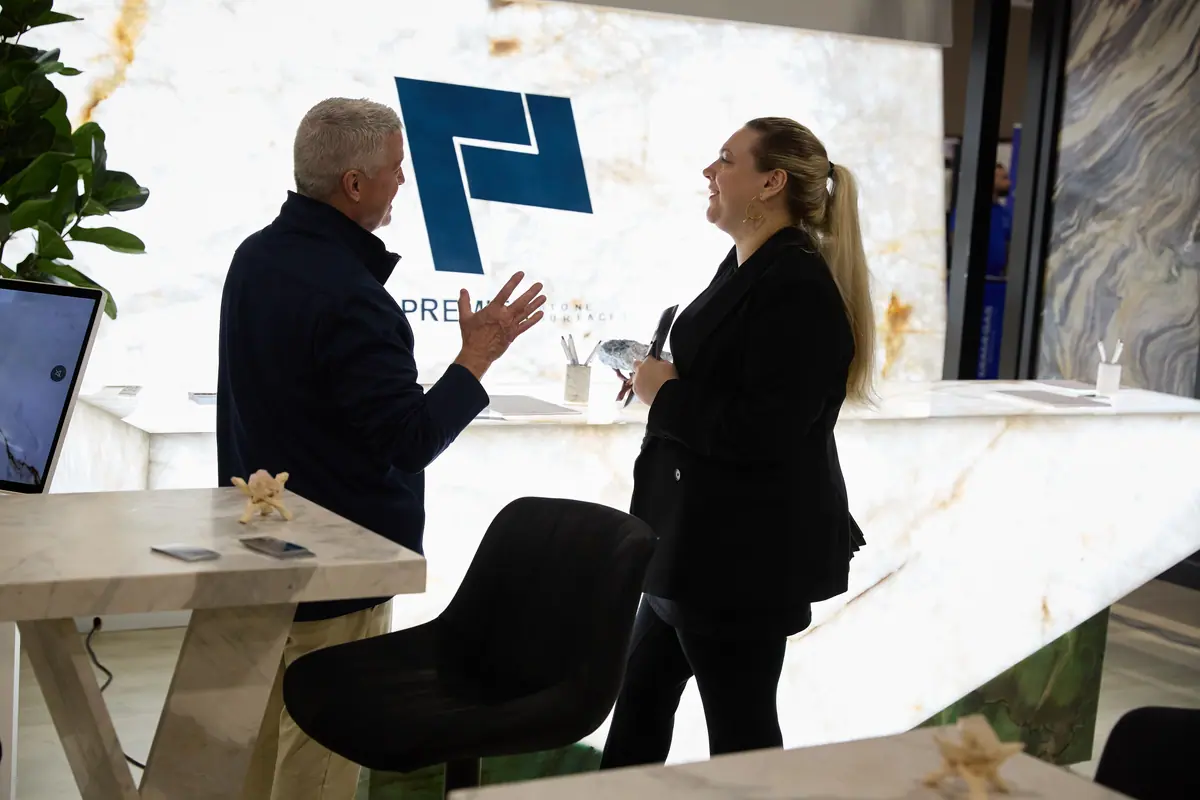Asistente y representante de un expositor conversan en una exhibición de alta gama de Premier Stone Surfaces en la feria del hogar