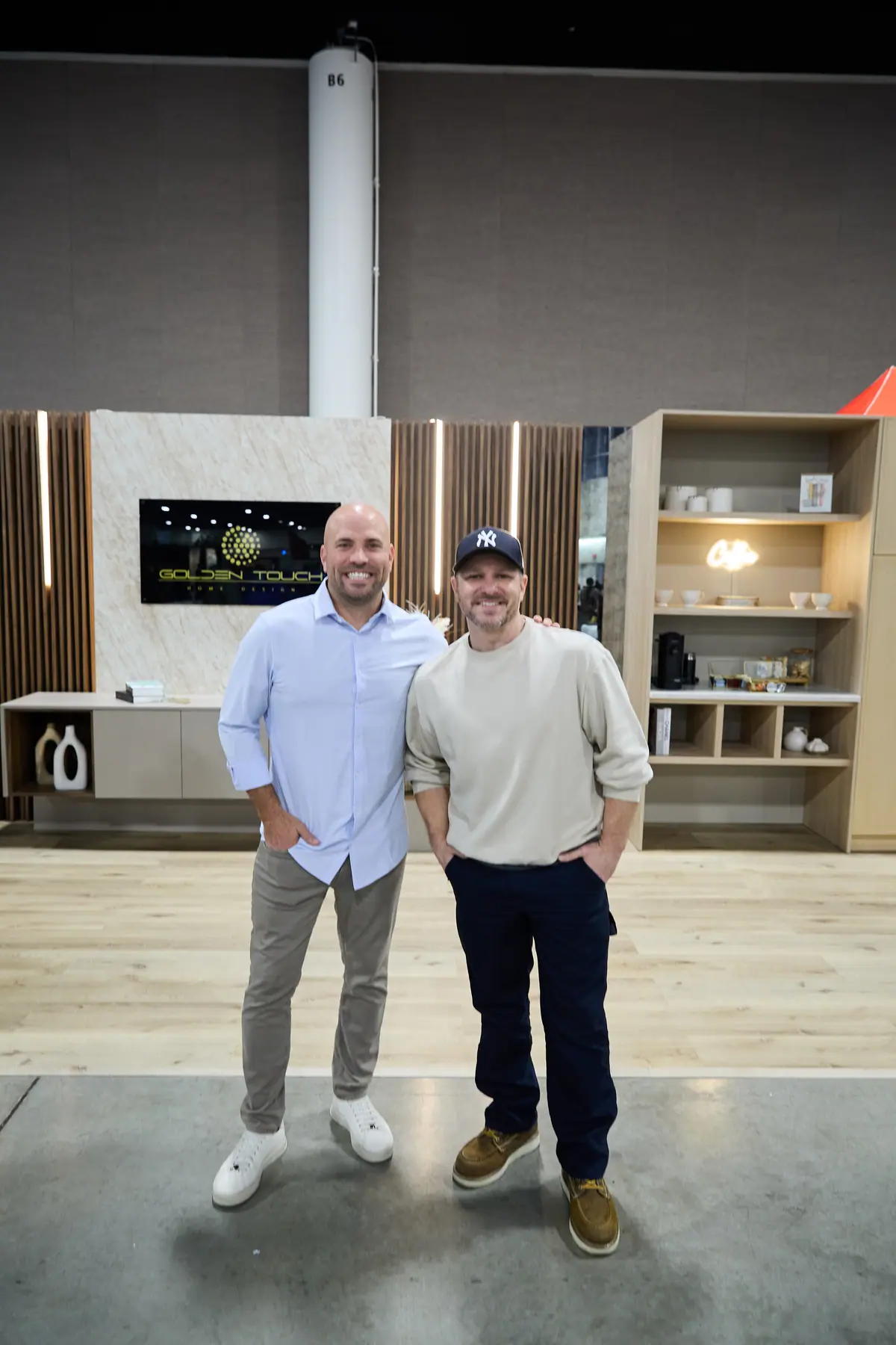 Two men pose together in front of a Golden Touch Home Design exhibit booth on the show floor