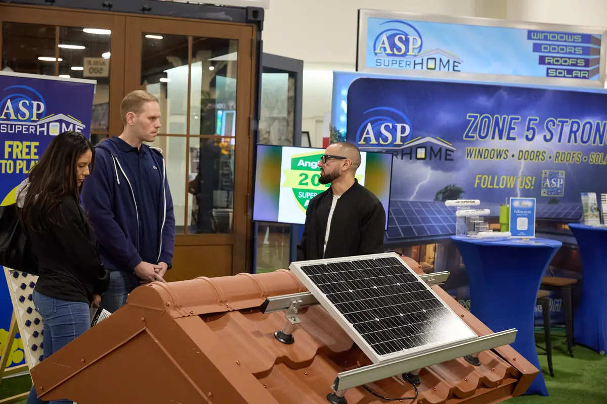ASP SuperHome exhibitor shows a solar panel and roof tile display to two visitors at the home show
