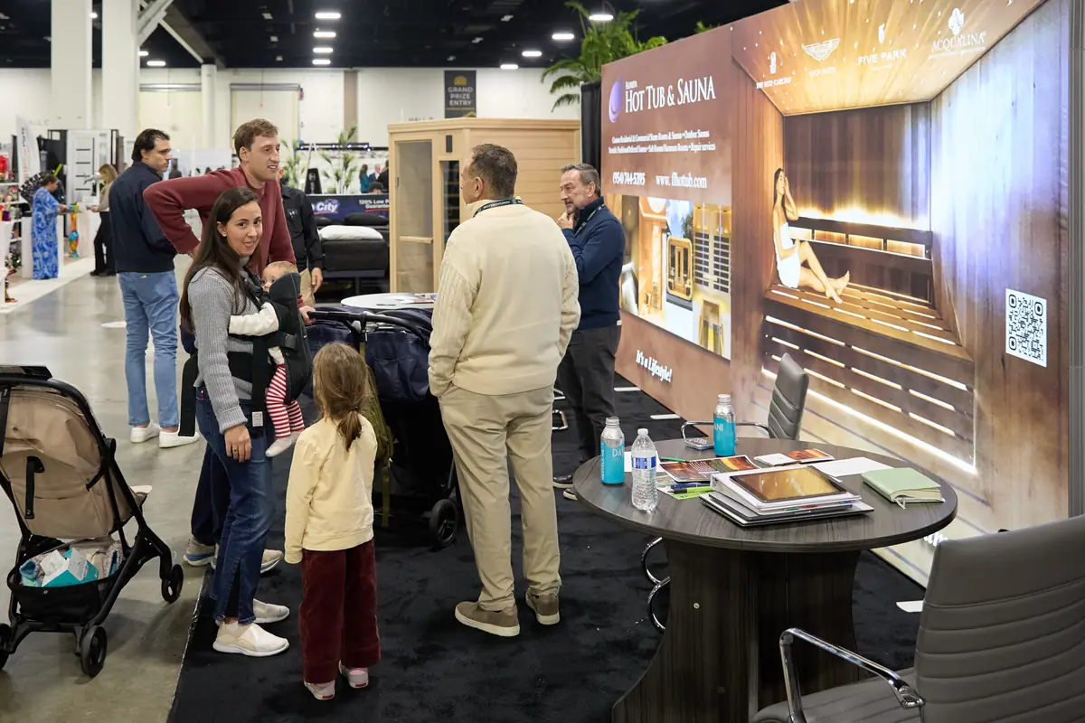 Family browses a Florida Hot Tub and Sauna exhibit with a cedar sauna cabin on display