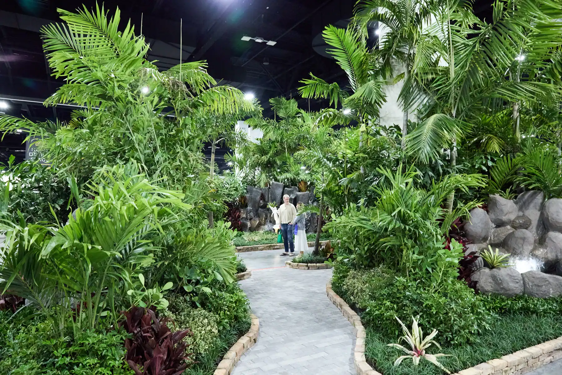 Lush indoor tropical garden display with palm trees, rock waterfall, and winding path at a Fort Lauderdale home show