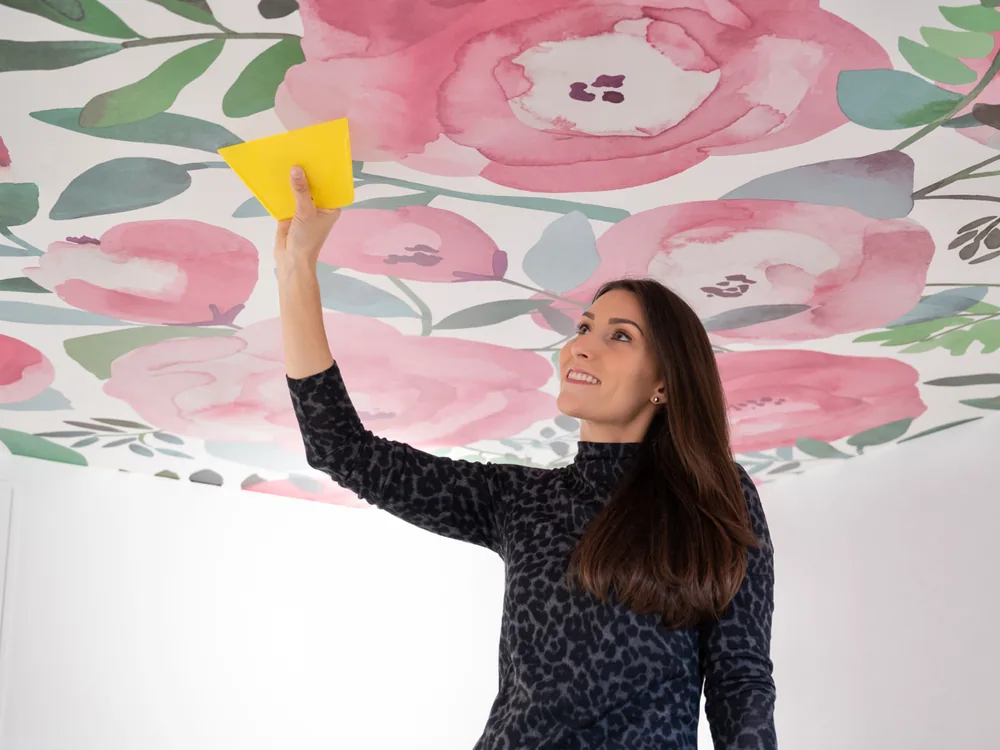 Katie Hunt smoothing a large-scale pink floral wallcovering across a ceiling