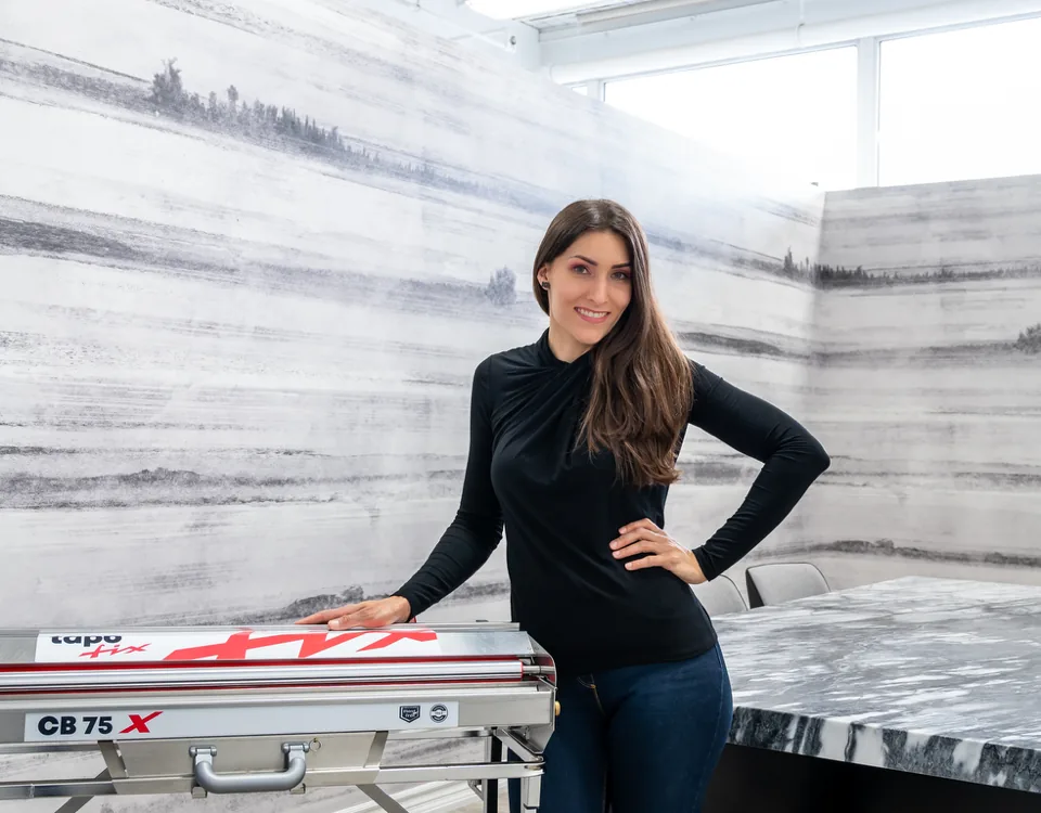 Katie Hunt beside her trimming table in a room wrapped in an ink-wash mountain landscape mural, installed as one continuous scene