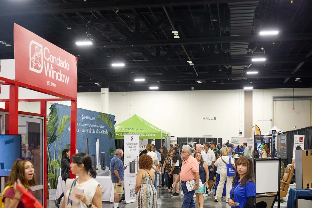 Crowds of attendees walk the convention hall aisle past a red 'Condado Window' booth and a green 'Hall B' tent sign under exposed black ceiling rigging, landscape orientation.