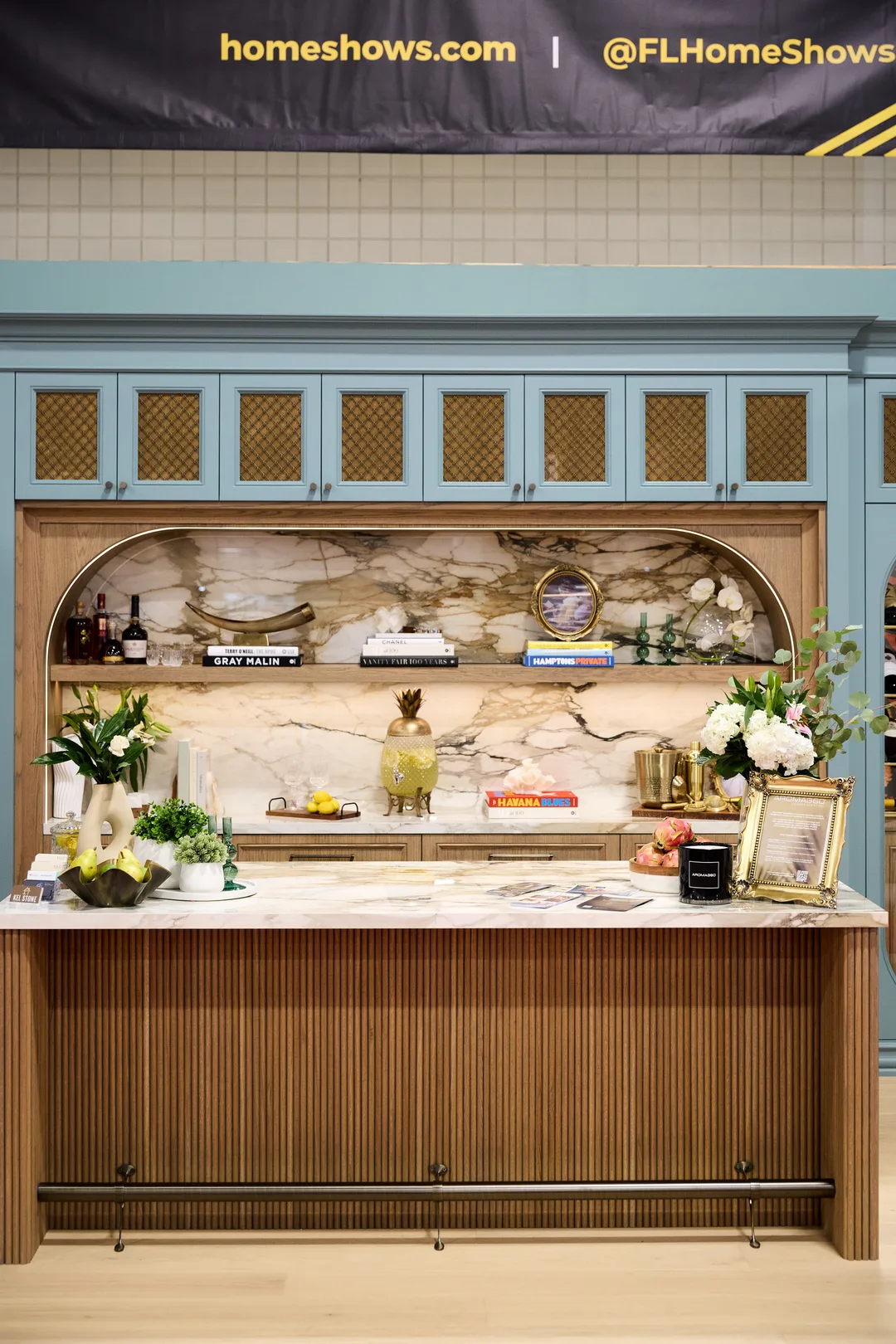 A teal butler's pantry with lattice-front upper cabinets, an arched marble-backed niche styled with coffee-table books and flowers, and a fluted wood bar front under a @FLHomeShows banner, portrait orientation.