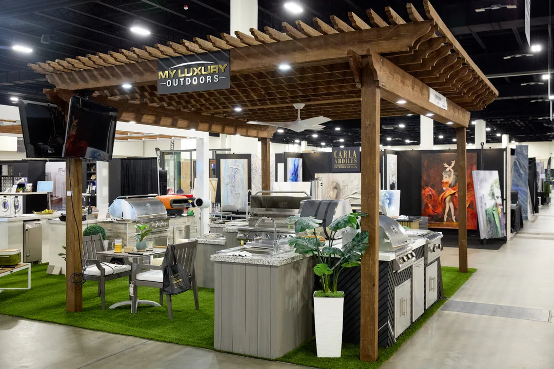 My Luxury Outdoors booth featuring a wood pergola over an outdoor kitchen with stainless grills, artificial turf and patio furniture.