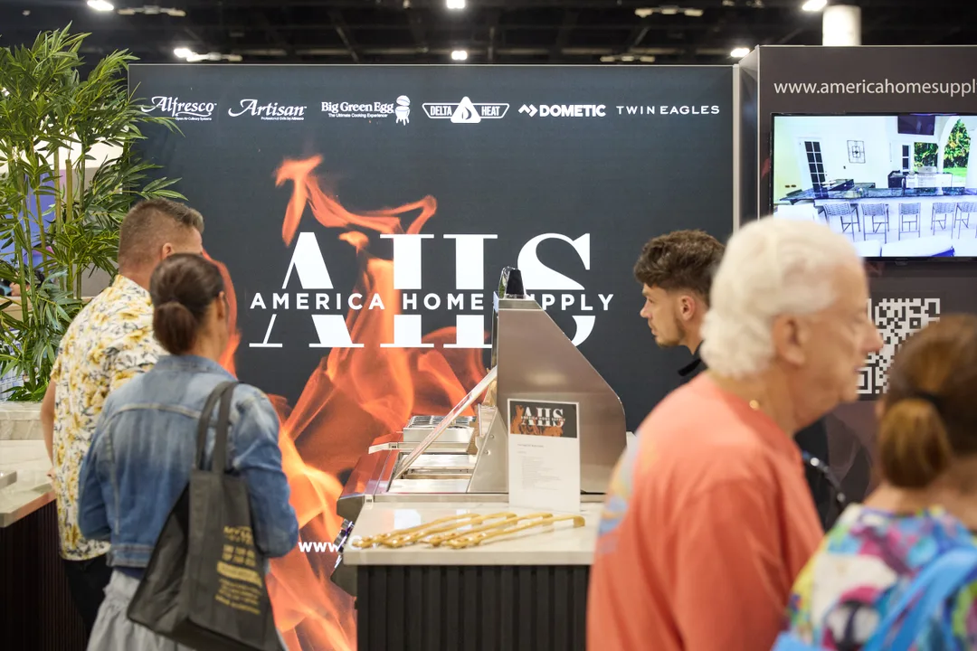 Attendees at the America Home Supply grill booth with a flame-graphic backdrop, an outdoor grill display and brand logos including Alfresco, Big Green Egg and Dometic.