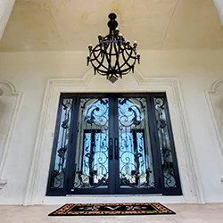 Ornate wrought-iron double entry doors with arched transom and chandelier above