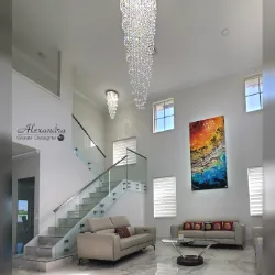 Two-story living room with glass staircase, chandelier, and large wall painting