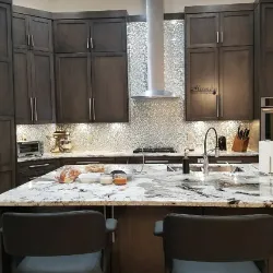 Kitchen with dark wood cabinets, marble island, and mosaic backsplash range hood