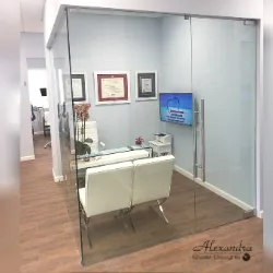 Glass-walled office consultation room with white chairs and framed certificates
