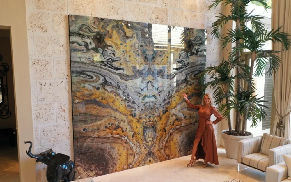 Designer posing beside a massive floor-to-ceiling abstract glass art installation in a luxury home