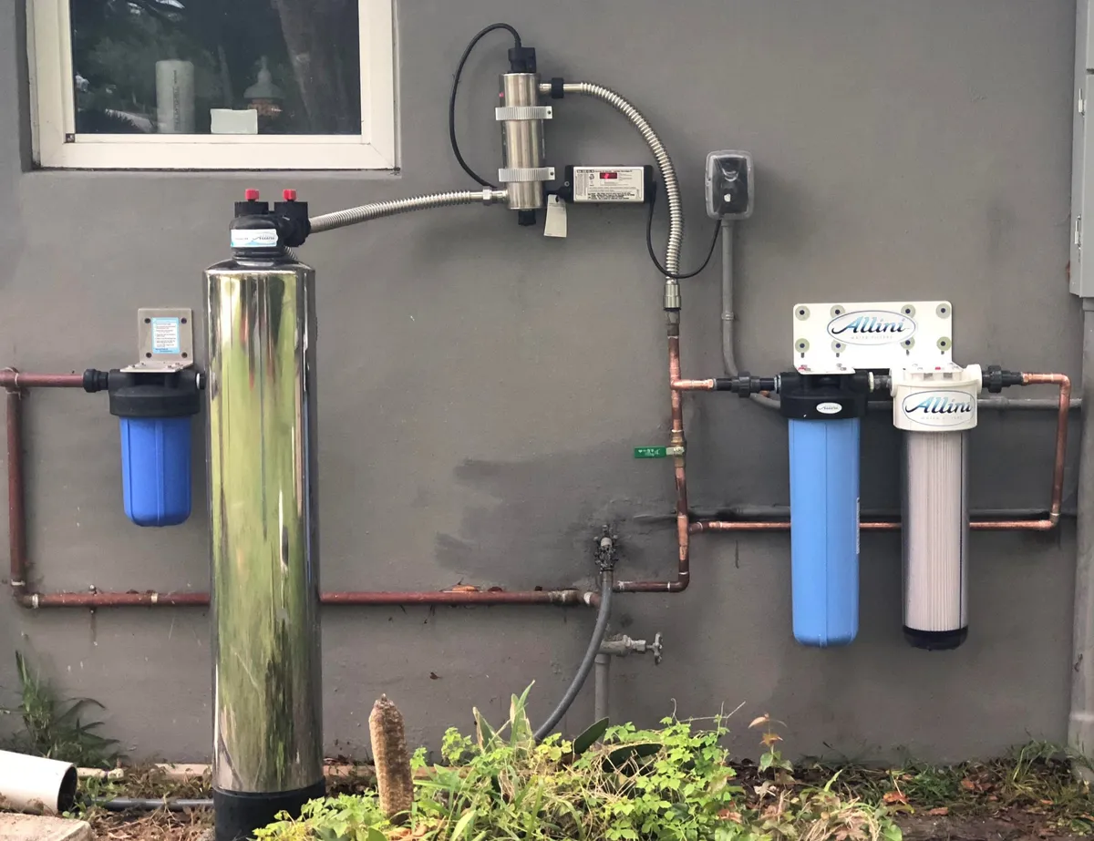 Allini whole-home filtration system with UV sterilizer and blue filter cartridges on grey wall