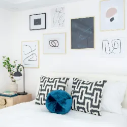 Bright white bedroom with gallery wall of framed art above a patterned pillow bed