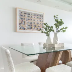 Glass-top dining table with curved wood base and white chairs in a bright room