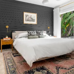 Moody bedroom with dark slat accent wall, white bedding, and botanical window view
