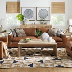 Coastal living room with tan leather sofa, geometric jute rug, and botanical wall art