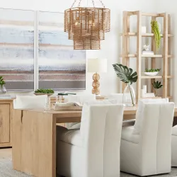 Bright dining room with white linen chairs, natural wood table, rattan chandelier, and tall shelving