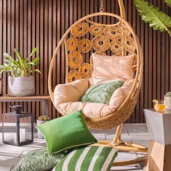 Woven rattan egg swing chair with peach cushions on a slatted wood patio