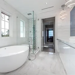 Freestanding oval soaking tub in bright white master bath with glass shower and chandelier
