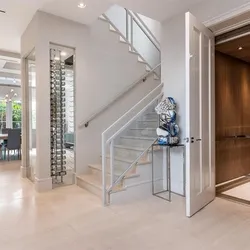 Custom home entryway with floating staircase, glass wine cellar, and wood-paneled elevator door