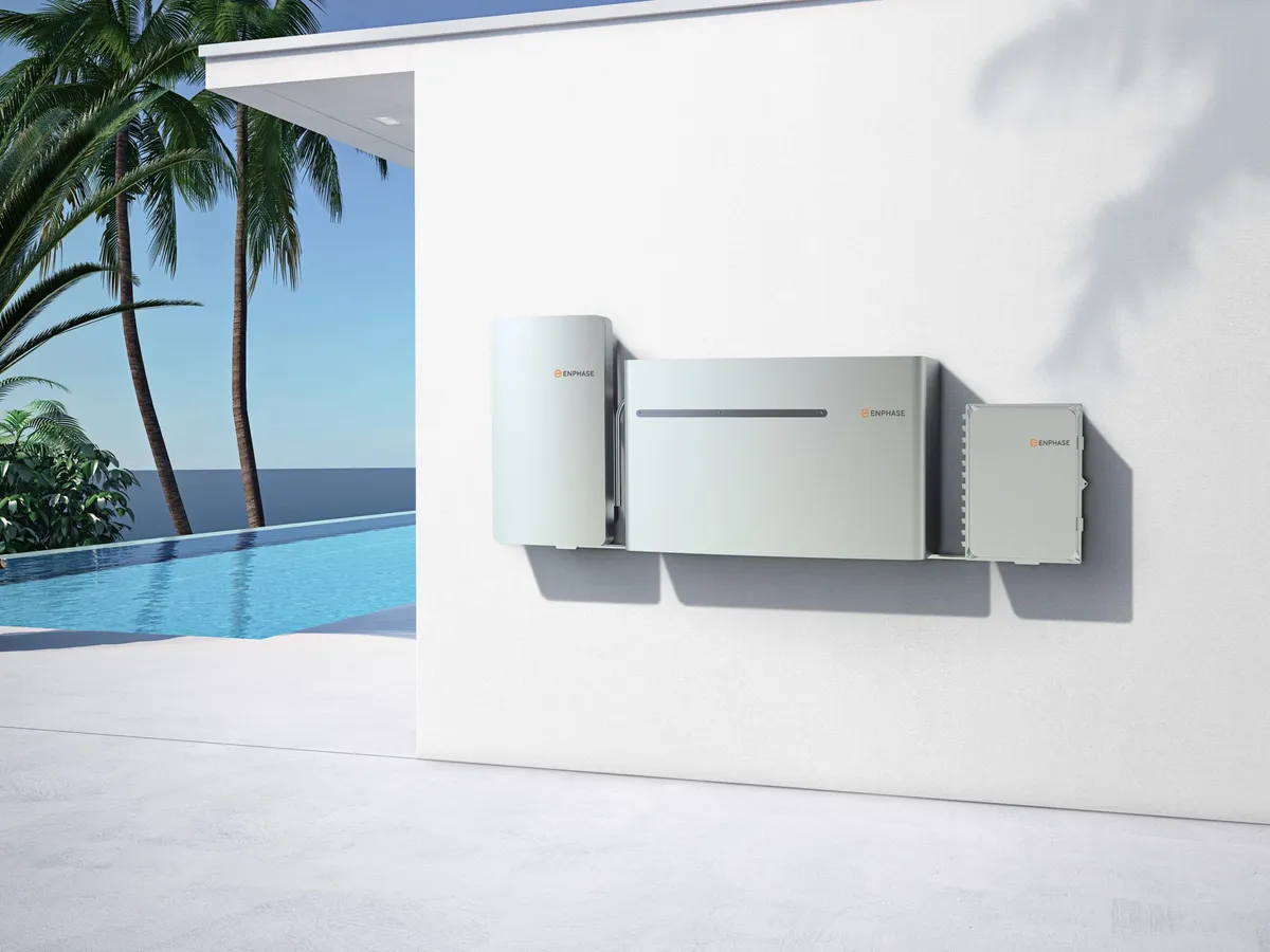 Enphase IQ battery and inverter system mounted on exterior wall of modern home with pool view