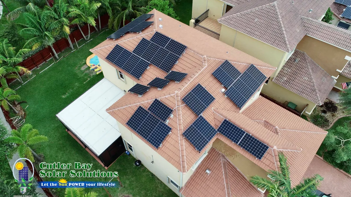 Aerial view of black solar panels on clay tile roof with pool, Cutler Bay Solar Solutions logo