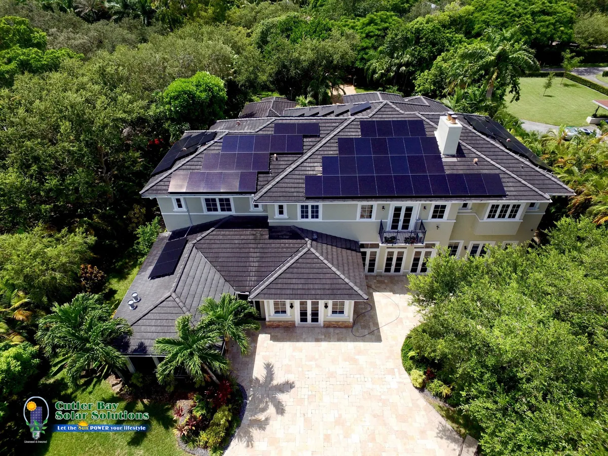 Aerial view of large Florida home with solar panels on multi-pitched roof amid tropical canopy, Cutler Bay Solar logo