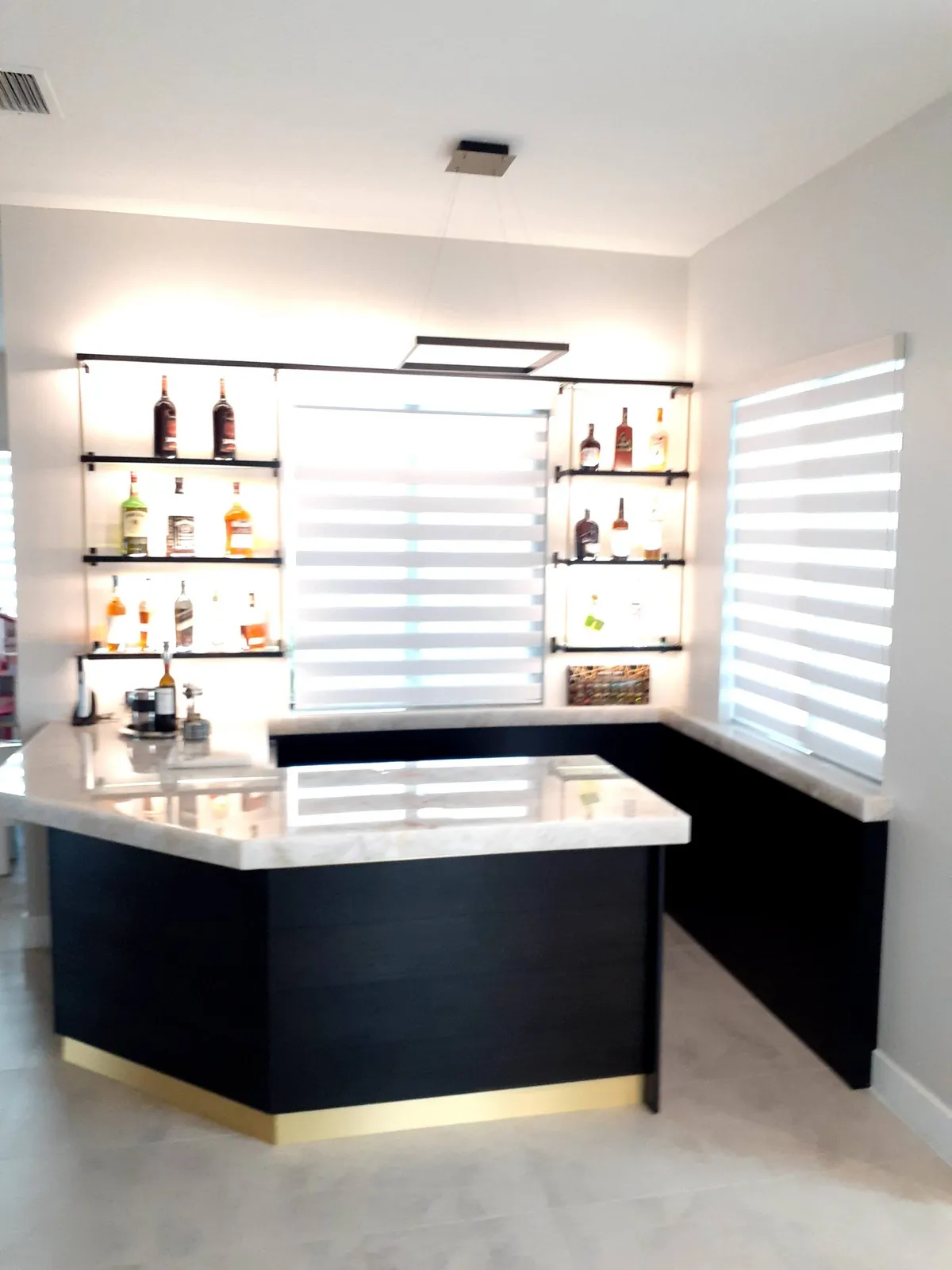 Modern L-shaped home wet bar with marble countertop and glass floating shelves