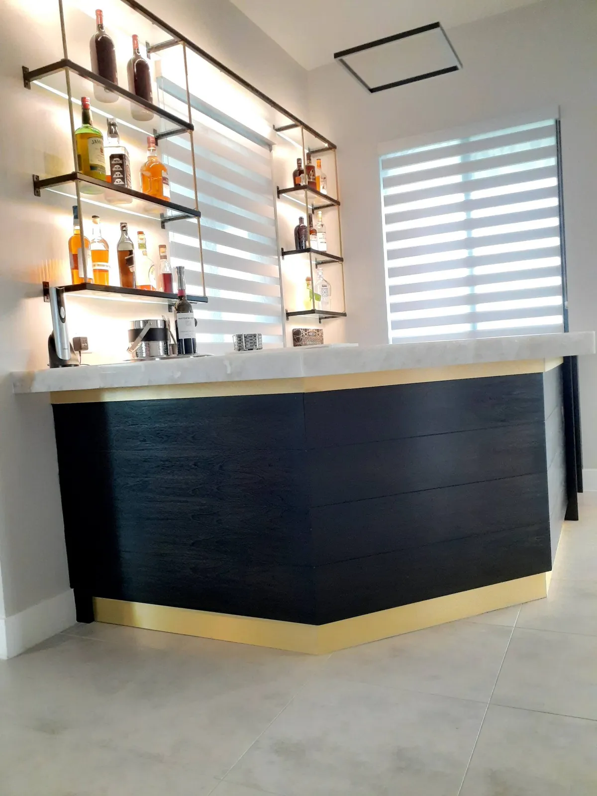 Custom dark wood bar with marble top, backlit shelves, and gold base trim