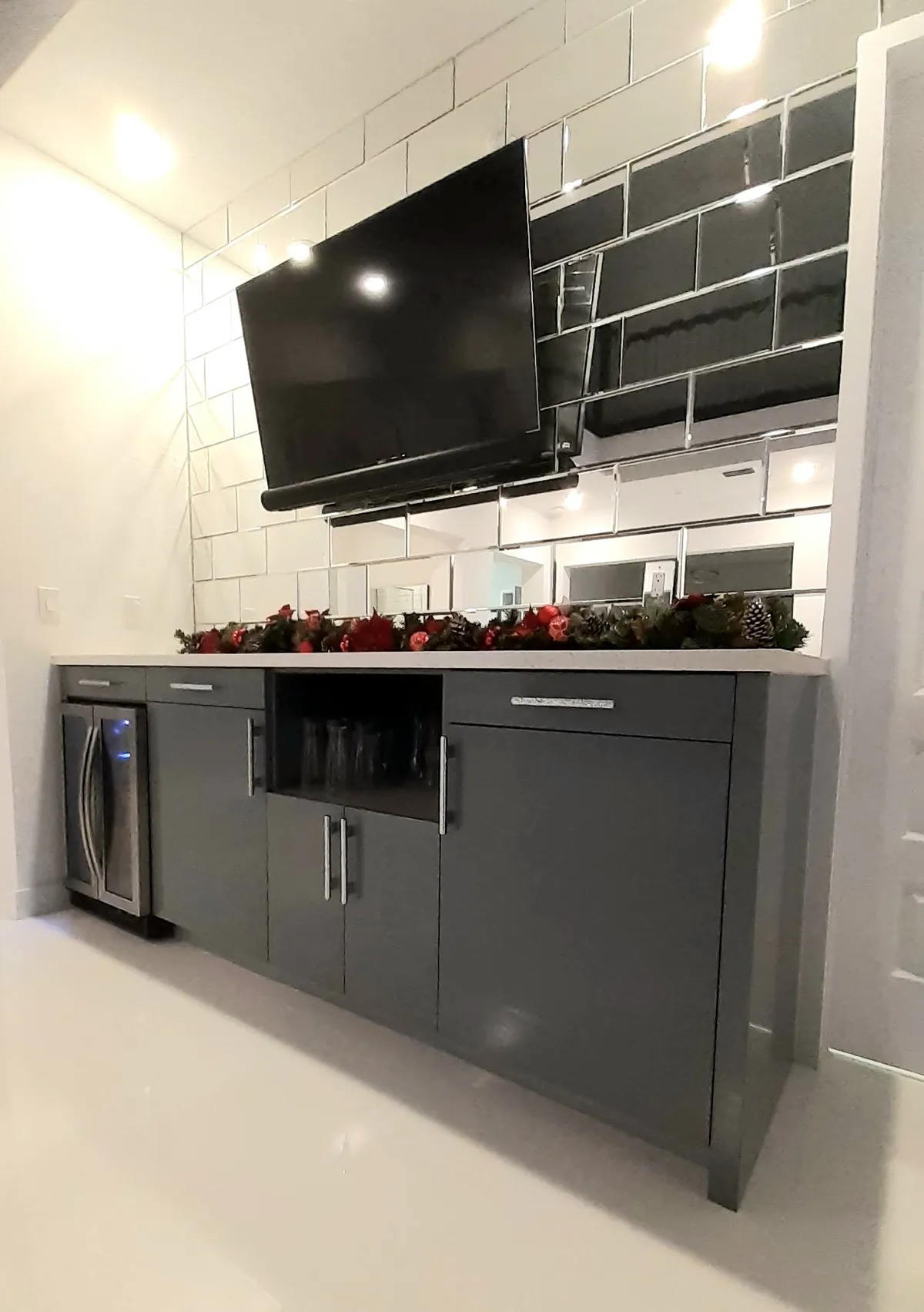 Built-in bar cabinet with mirrored tile backsplash, wine fridge, and mounted TV