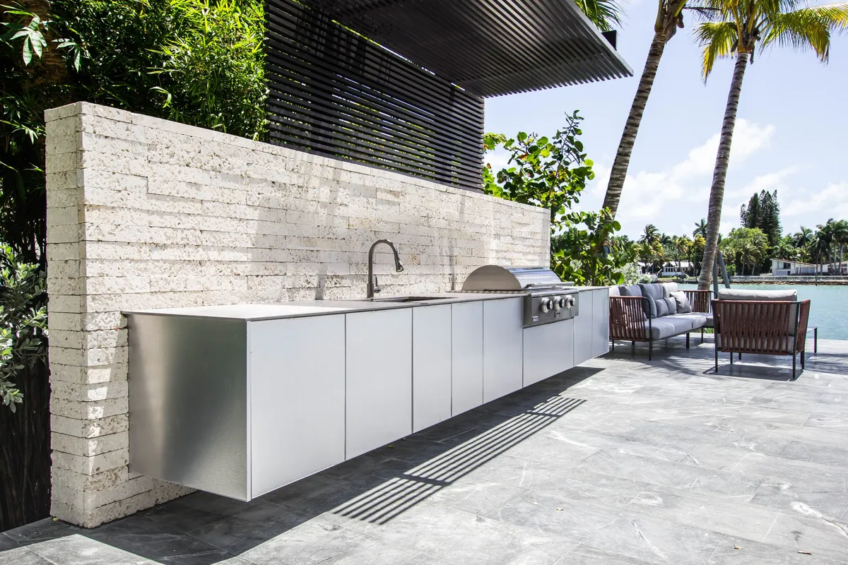 Stainless steel outdoor kitchen with natural stone backsplash and pool view