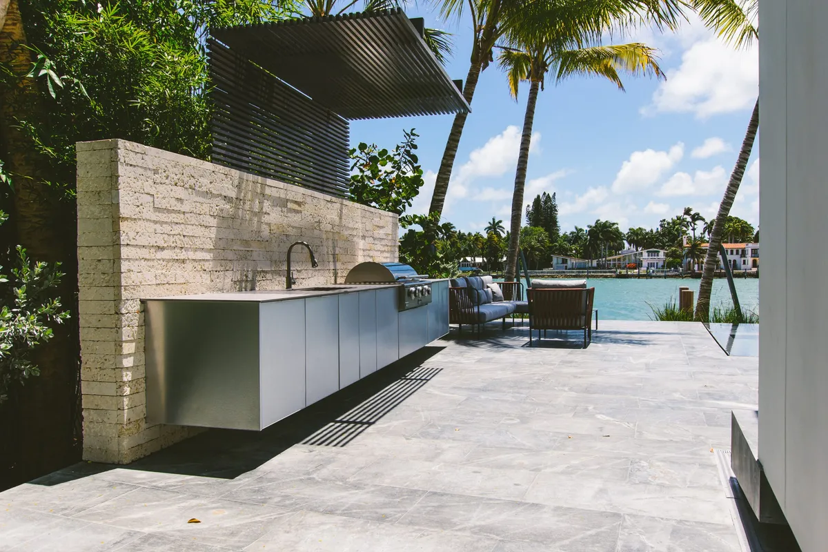 Outdoor kitchen with stone pizza oven, stainless cabinets, and waterfront pool