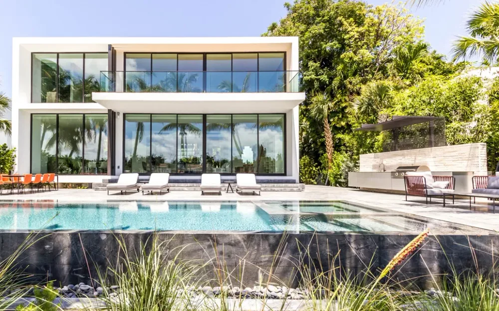 Contemporary glass home with infinity-edge pool and tropical landscaping at dusk