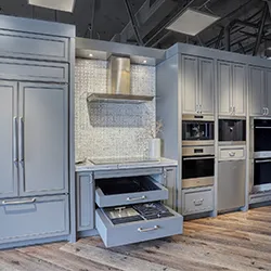 Appliance showroom display of gray cabinetry with built-in ovens and refrigerator columns