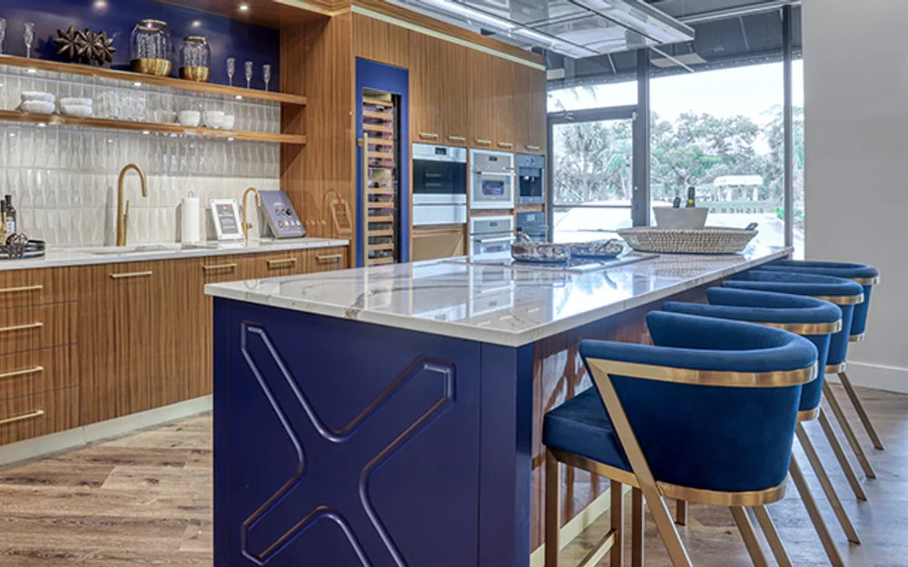 Luxury kitchen showroom with navy island, walnut cabinetry, and blue bar stools