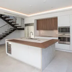 Modern white kitchen with wood-tone island, built-in stainless appliances, and floating staircase