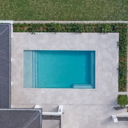 Aerial view of rectangular pool with large-format gray tile surround and green lawn