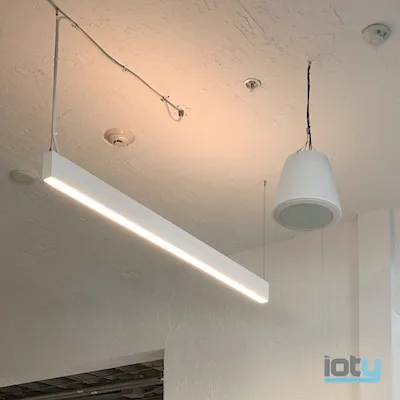 Suspended linear LED light fixture and pendant speaker on white textured ceiling