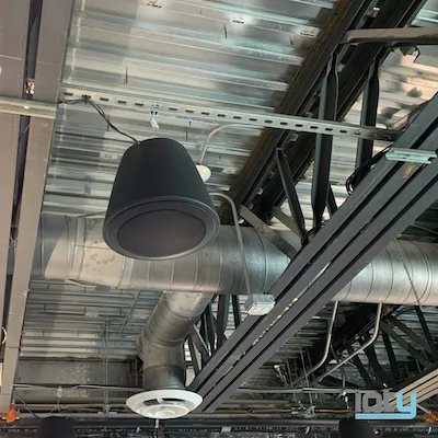 Black architectural ceiling speaker mounted among HVAC ducts and structural beams