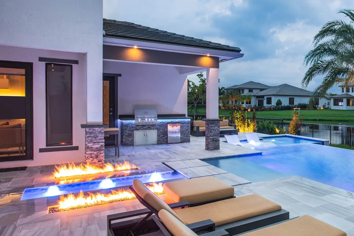 Luxury backyard at dusk with fire features, pool, outdoor kitchen, and fire pit