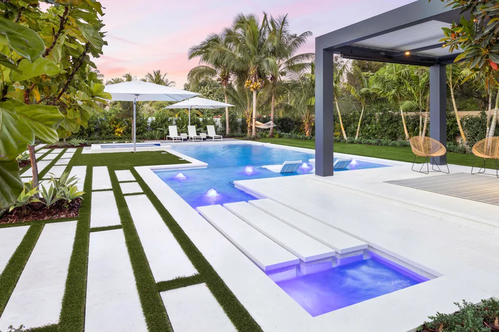 Resort-style pool with spa, pergola, palm trees, and turf pathways at sunset